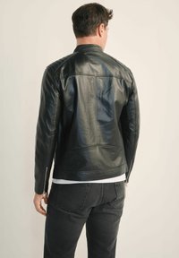 Czarna skórzana kurtka o slim fit, z kołnierzem stojącym, detalami zamka błyskawicznego na rękawach oraz subtelnymi przeszyciami. Nosi się ją na ciemnych dżinsach.