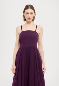 Mauve haljina bez rukava s kvadratnim izrezom i plisiranim suknjom. Izrađena od glatke tkanine s uskim trakama. Elegantna silueta i minimalistički dizajn.
