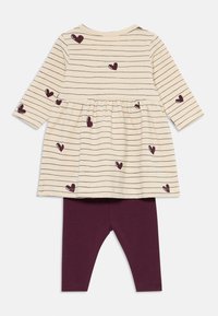 Gestreiftes cremefarbenes Kleid mit kastanienbraunen Herzmotiven, gerafftem Taillenbund und langen Ärmeln, kombiniert mit einfarbigen kastanienbraunen Leggings. Aus Baumwollmaterial.