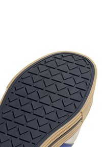 La suola delle scarpe presenta un battistrada in gomma nera con un motivo a forma triangolare e un bordo beige, che indica resistenza e aderenza.