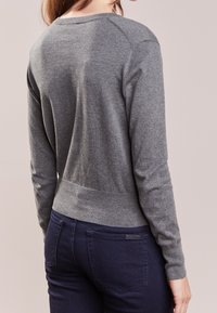 Harmaa pitkähihainen neule, jossa resorit hihansuissa ja helmassa, sileä pinta. Yhdistetty tummansinisiin farkkuihin, korostaen vartalonmyötäistä siluettia.