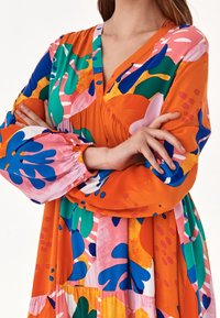 Färggklad klänning med en orange bas och abstrakta mönster i blått, rosa, grönt och gult, långärmad och med V-ringning.