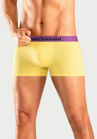 Yellow boxer shorts with a purple waistband featuring "nano banani" logo. Made of smooth fabric, fitted design, and mid-thigh length.