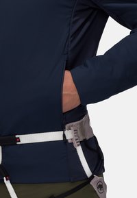 Navy zippered softshell jacket with stretch fabric; features a harness underneath and adjustable waistband with white straps.