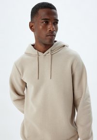 Sudadera con capucha beige hecha de una tela suave con un corte relajado, que cuenta con capucha ajustable y mangas largas.
