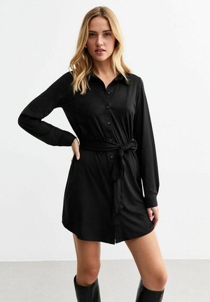 Robe noire à manches longues, avec un ceinturon à la taille, une texture lisse et une longueur en dessous du genou.