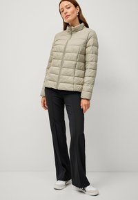 Chaqueta de plumas gris claro con collar alto y acolchado horizontal, combinada con pantalones acampanados negros y zapatillas blancas. Paleta de colores neutros.