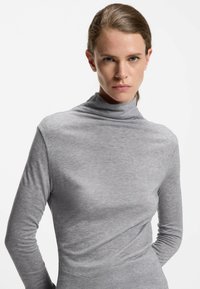 Grijze coltrui van zacht, glad materiaal, met lange mouwen en een getailleerde pasvorm. Minimalistisch ontwerp zonder patronen.