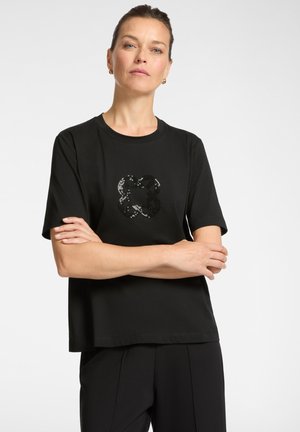 Schwarzes T-Shirt mit kurzen Ärmeln aus weichem Stoff, mit einem graphischen Design aus schwarzen und silbernen Pailletten auf der Vorderseite. Lockere Passform, schlichter Ausschnitt.