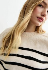 Maglione beige con strisce orizzontali nere, texture lavorata a maglia, scollatura rotonda e dettagli a coste ai polsini e all'orlo. Tessuto morbido.