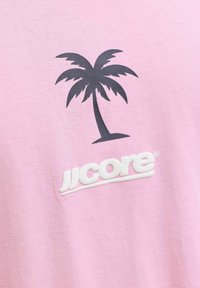 Graphique de palmier noir au-dessus du texte blanc "JJcore" sur tissu rose clair.