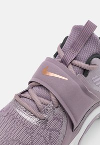 Fioletowy sneaker Nike z teksturowaną cholewką z siateczki, gładkim paskiem z metalicznym logo oraz amortyzowaną podeszwą.