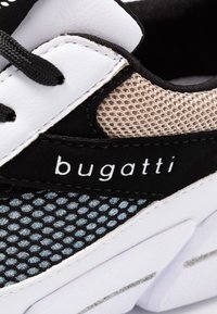Sneaker in bianco e nero con tomaia in mesh strutturato, dettaglio beige, lacci neri e logo ben visibile sul lato.
