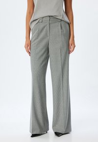 Pantalons larges à motif à carreaux gris fabriqués en tissu texturé, avec une taille haute et des plis sur mesure. Accentués avec des chaussures noires.