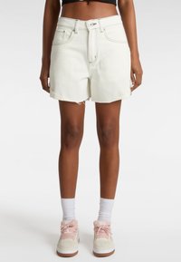 Shorts en denim de couleur claire avec une taille haute, un ourlet brut et des coutures contrastées. Associés à des chaussettes blanches montantes et des baskets roses.