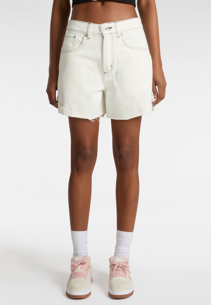 Shorts en denim de couleur claire avec une taille haute, un ourlet brut et des coutures contrastées. Associés à des chaussettes blanches montantes et des baskets roses.