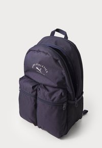 Mochila de tela azul marino con dos bolsillos frontales con cremallera, forma redondeada y correas de hombro ajustables. Presenta un logo de la marca en la parte superior.