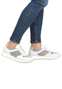 White athletic shoes with mesh panels and green accents, featuring a cushioned sole and rounded toe. Worn with denim jeans.