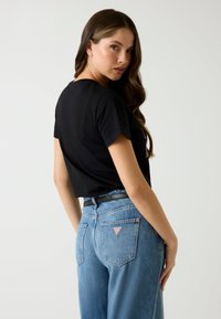 Zwarte kortebloemige cropped t-shirt gecombineerd met hooggerande lichtblauwe denim jeans met een klein rood driehoeklogo op de achterzak.