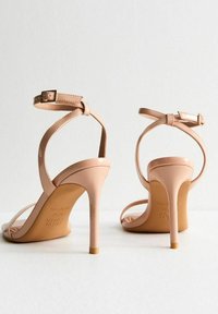 Nude patenten leren hoge hakken sandalen met dunne enkelbandjes, open teen en een slanke hak, met een gouden accent op de basis van de hak.