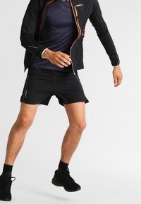Svart löparjacka med orange accenter, kombinerad med svarta shorts. Outfiten har en lätt design och atletisk passform för rörelsefrihet.