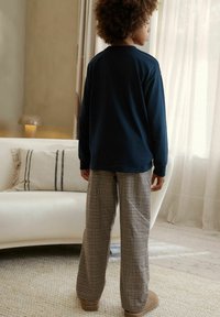 Tumesinise tooniga pikad varrukad vaba lõikega särk, kombineeritud beežides ruudulistes lameda lõikega pükstega ja pruunide sussidega. Neutraalsetes toonides sisustusega interjöör.