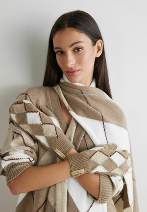 Beiger und weißer Pullover mit Rautenmuster, um einen passender hellbrauner Schal gewickelt; fingerlose Handschuhe mit markanten Logotags.