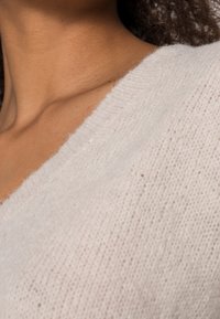 Lys beige striktrøje med et blødt, struktureret stof. Har en bred V-halsudskæring og en løs pasform, der fremhæver dens fine, lette design.