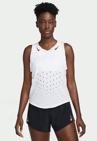 Fehér sportos ujjatlan felső, V-nyakkivágással, perforált mintázattal a szellőzés érdekében, fekete sorttal párosítva, mindkettő Nike márkajelzéssel.