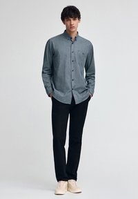 Lätt, knappad skjorta i melerat grått tyg, med bröstficka och skräddarsydd passform, tillsammans med svarta byxor och ljusa sneakers.