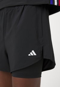 Pantalones cortos deportivos negros hechos de un tejido ligero, con un logo de Adidas blanco, cintura elástica y aberturas laterales para mayor movilidad.