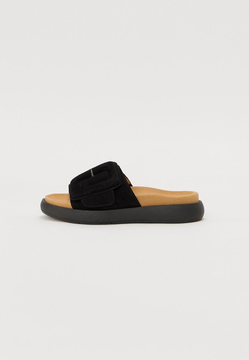 Black suede slide sandals featuring a wide strap and a cushioned tan footbed, with a flexible black rubber sole.