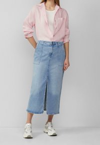 Chemise en lin rose pâle à boutons, débardeur blanc en dessous, associée à une jupe en jean mi-longue avec une fente frontale et deux poches.