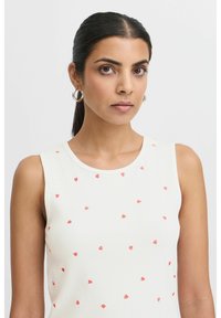 Débardeur blanc à côtelés avec de petits motifs de cœurs rouges dispersés, col rond et sans manches.
