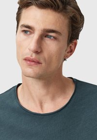 Mörkt grön bomulls-T-shirt med rund halsringning, korta ärmar och en slät yta. Har subtil sömnad runt halsringningen.