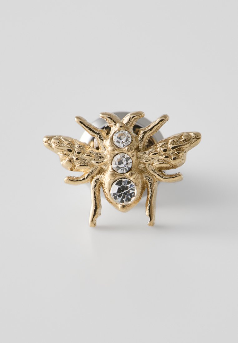 Anello a forma di ape in tonalità oro con tre strass trasparenti sul corpo e dettagli intricati sulle ali e sulle gambe. Banda in metallo liscia.