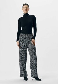 Zwarte coltrui gecombineerd met wijde broek in een grijs en zwart luipaardpatroon. Model draagt puntige zwarte hakken.