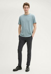 Tricou de culoare albastru deschis, cu guler rotund, realizat dintr-un material moale, asortat cu pantaloni negri slim-fit și botine negre cu șireturi.