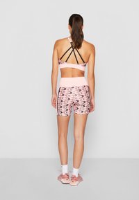 Reggiseno sportivo rosa con spalline nere e pantaloni corti a vita alta rosa abbinati, caratterizzati da un motivo ondulato in nero e rosa. Footwear di un rosa chiaro.