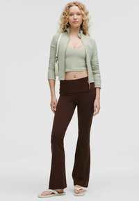 Light green zip-up jacket, matching crop top, and brown flared pants. Textured fabric, with a smooth finish and light sandals. Minimalist design.