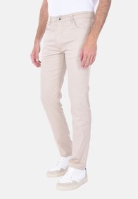 Chinos beige con una vestibilità slim, realizzati in un tessuto liscio. Presentano tasche anteriori, chiusura con bottone e un classico design a cinque tasche.