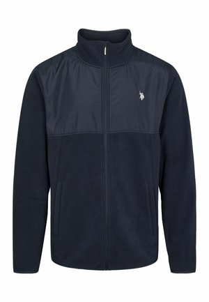 Sötétkék polárdzseki kontrasztos nejlonpanellel a tetején, cipzárral, állógallérral és oldalsó zsebekkel. Apró logó található a mellkasán.
