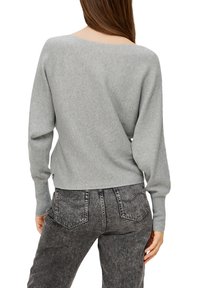 Grauer gerippter Pullover mit weitem Ausschnitt und langen Ärmeln, kombiniert mit hochgeschnittenen dunkelgrauen Jeans. Subtile strukturelle Details im Stoff.