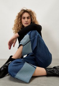 Pantaloni in denim a gamba larga con orli sfrangiati; presentano un pannello di contrasto azzurro chiaro. Abbinati a stivali neri alla caviglia e a un top nero a coste.