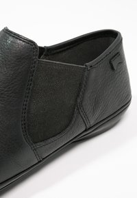 Zapato de cuero negro con paneles laterales elásticos, diseño redondeado, acabado texturizado y un pequeño acento de logo. Apto para uso casual.