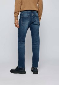 Modré džínové kalhoty s přiléhavým střihem, s kapsami na zadní straně, středně vysokým pasem a mírným opráním, doplněné černými botami.