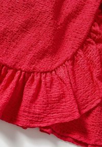 Pomarszczony czerwony materiał z falbaniastym wykończeniem, posiadający teksturowaną powierzchnię i gładkie wykończenie. Projekt jest miękki i zwiewny.