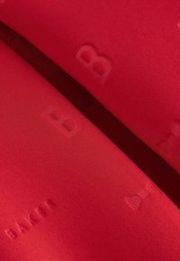 Gros plan d’un tissu rouge avec des motifs embossés subtils, incluant le mot "BARIII" et des formes de nœuds papillon.