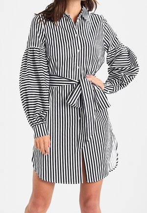 Czarna i biała sukienka w paski zapinana na guziki, z balonowymi rękawami, paskiem w talii i długością do połowy uda z bocznym rozcięciem.