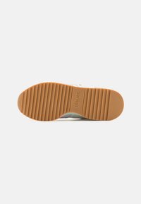 Suola della scarpa con texture rigata, realizzata in gomma; presenta un colore beige con impressa un logo. Il lato superiore liscio si trasforma nella suola inferiore.